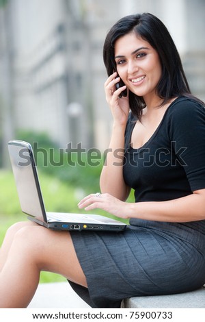 An attractive Indian businesswoman sitting outside with laptop and phone
