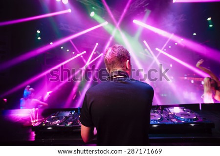DJ with headphones at night club party under the blue light and people crowd in background