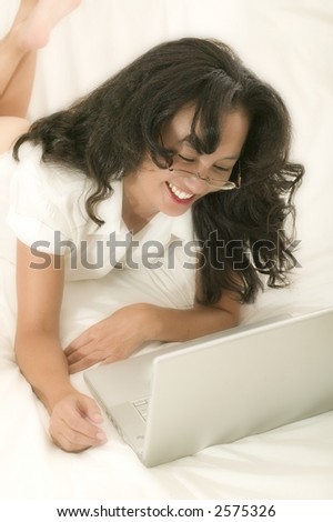 An attractive young asian woman works on her laptop whilst still in bed