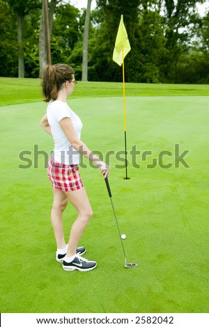 A young woman considers her shot on the putting green of a golf course.  Model Released.
