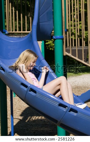 A young blond girl plays on the slide at a local park.