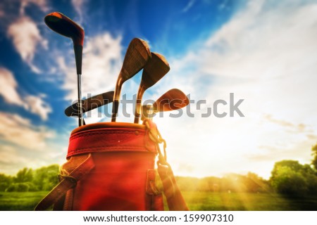 Golf equipment. Professional golf clubs in a leather baggage at sunset