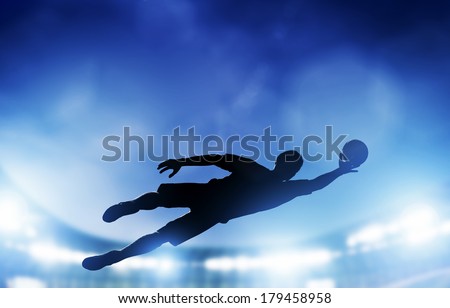 Football, soccer match. A goalkeeper jumping to defend, save the ball from goal. Lights on the stadium at night.