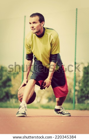 Young man on basketball court dribbling with ball. Streetball, training, activity. Real and authentic, vintage mood.