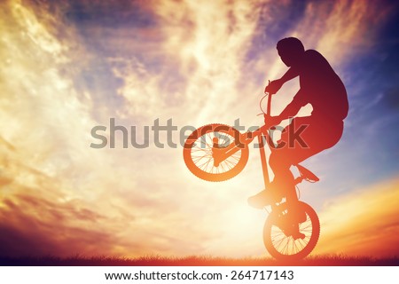 Man riding a bmx bike performing a trick against sunset sky. Extreme sport