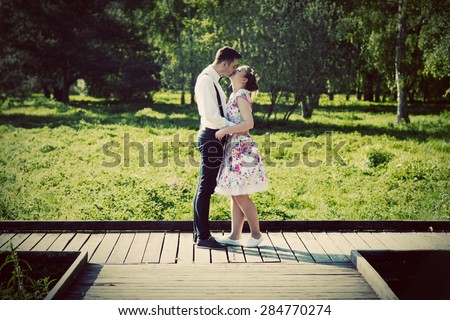 Young couple in love standing on wooden cross-roads in summer park. Woman in dress and man wearing shirt with suspenders.
