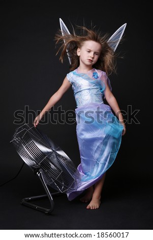 Cute little girl in blue fairy dress posing in strong stream of air.