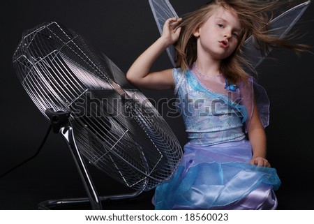 Beautiful little girl in blue costume and wings posing in strong stream of air.