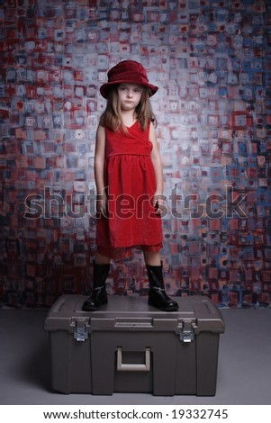 Beautiful sad little girl in red dress standing on a box.