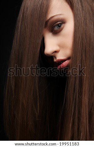 Beautiful young woman with long healthy dark hair on black background.