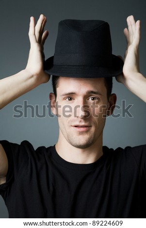 Young handsome man in black shirt holding black hat.