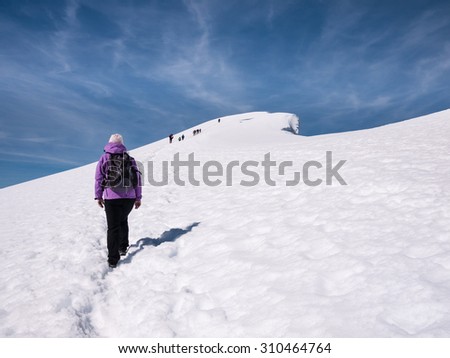 Persons approaching a famous permanent snow covered mountain summit in Norway during a day With sun at summer walking at a snow covered glacier