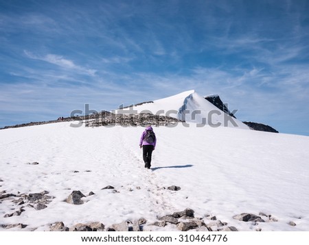 Female approaching a famous permanent snow covered mountain summit in Norway during a day With sun at summer walking at a snow covered glacier