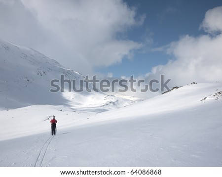 Woman skiing alone in a valley with various lighting conditions and mountain summits and clouds in the background in the norwegian mountains
