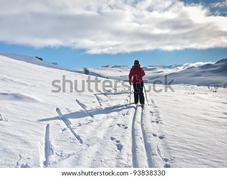 Woman skiing alone in an old ski track with new fallen snow heading towards a mountain summit at easter in the norwegian mountain at Laerdal