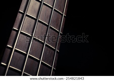 Detail of the fret board of a bass guitar, on a dark background.