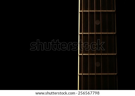 Detail of the fret board of an acoustic guitar, on a dark background.