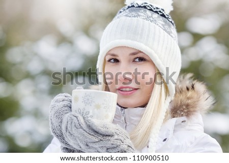 A young girl in warm winter clothes holding a cup with a drink on the background of the winter forest, horizontal frame, close up portrait