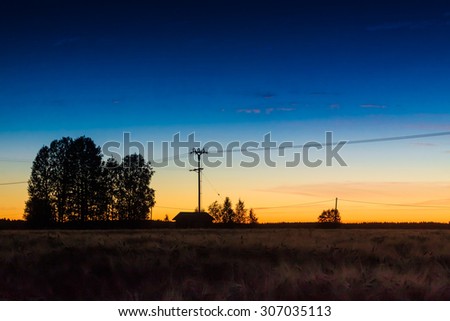 The sun sets behind the little barn and the telephone lines in the Northern Finland on an early autumn night.