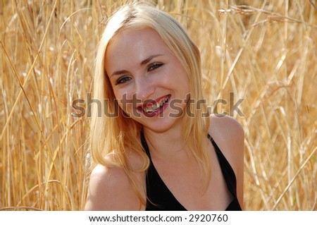 Portrait of a blonde woman with green eyes smiling, on a sunny day in grassfields.