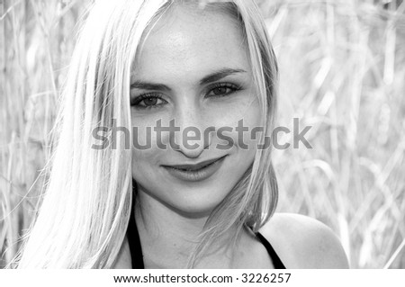 Portrait of a blonde woman with green eyes smiling, on a sunny day. Black and white image.