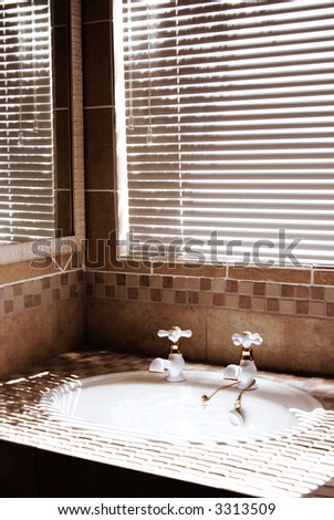 Modern bathroom with blinds on the window. Shot in the morning, with bright sun coming through the blinds. Artistic grain added to dramatize the interior.