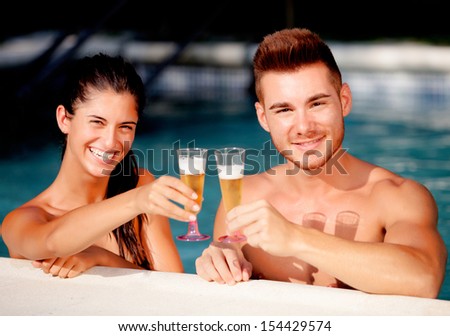 Happy couple relaxing in the pool in the summer celebrating their anniversary with champagne