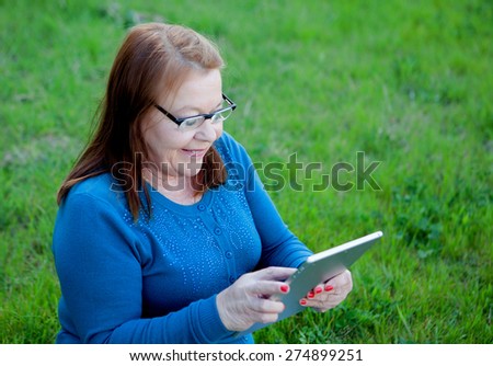 Elderly woman using a tablet while relaxing in the garden