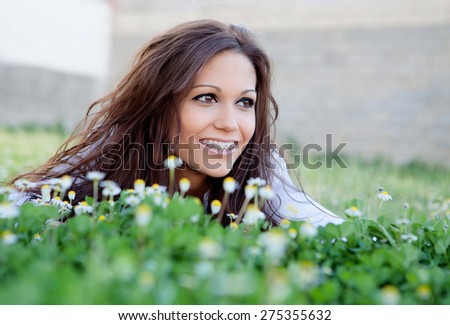 Brunette cool girl with brackets lying on the grass with many flowers