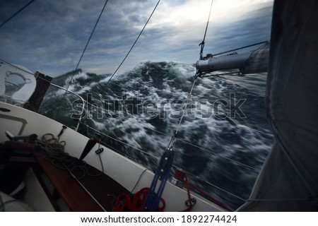 Heeled yacht sailing in the sea during the storm, a view from the cockpit. Dark waves, water splashes. Long exposure, motion. Rough weather, cyclone, danger, epic seascape. Regatta, racing, sport
