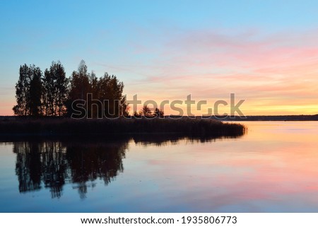 Epic red and golden clouds above the forest lake at sunrise. Dramatic cloudscape. Symmetry reflections on the water, natural mirror. Idyllic rural scene. Gauja national park, Sigulda, Latvia