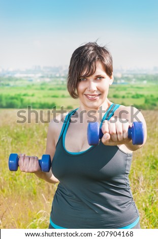 Beautiful plus size woman exercising with dumbbells outdoor