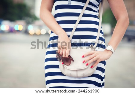 Fashionable woman with white bag in her hands and striped dress in the city