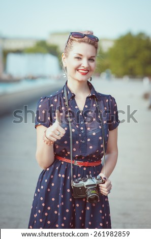 Beautiful young woman in vintage clothing with retro camera showing thumbs up outdoor