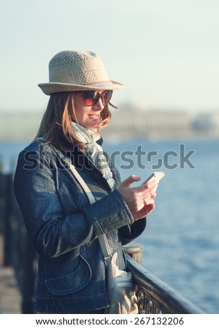 Beautiful young woman in hat and scarf with mobile phone outdoor in the city
