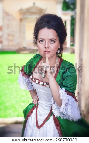 Beautiful young woman in green medieval dress making silence gesture outdoor