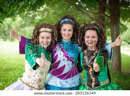 Three young beautiful girls in irish dance dresses showing thumbs up outdoor