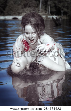 Beautiful vampire woman dressed white bloody shirt and her victim standing in the river