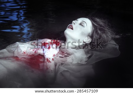 Young beautiful drowned woman in bloody dress lying in the water outdoor
