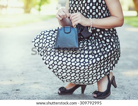 Fashionable woman with small bag in her hands and dress sitting outdoor