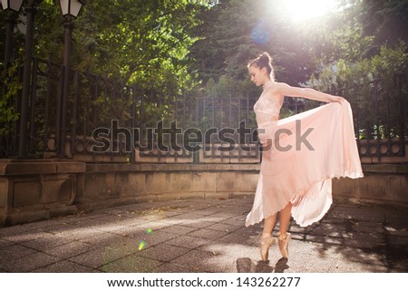 Young beautiful woman in elegant pink dress and ballet shoes in the garden.