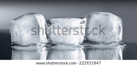 Three ice cubes with reflection on grey gradient background.