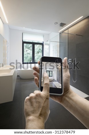 Mobile device with man hands taking picture in  tiled bathroom with windows towards garden, hands on the right side