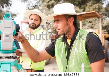 two civil engineers doing land survey at a construction site with construction machinery in the background