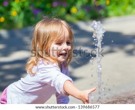 Cute little girl trying to catch the water from the fountain