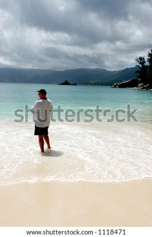 Man sanding on the beach in Seychelles looking out to sea and watching a storm coming in.