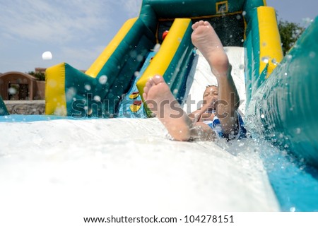 Splash! Young boy sliding down an inflatable water slide feet first while splashing water.