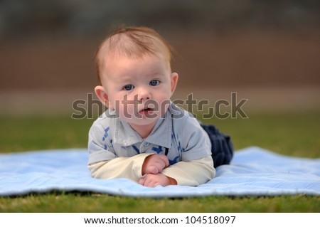 Infant Boy Laying on Front Outside. Infant three-month old boy laying on a blanket outside while looking at the viewer. Shallow DOF.