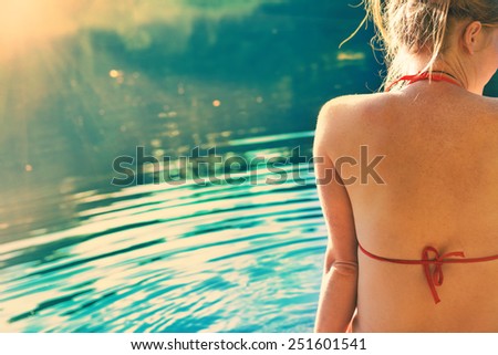 Back view portrait of a beautiful relaxed woman on the beach with blue water background. Colorized like instagram filter.