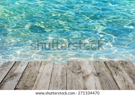 View from empty wooden deck table to tropical sunny beach with blue water background